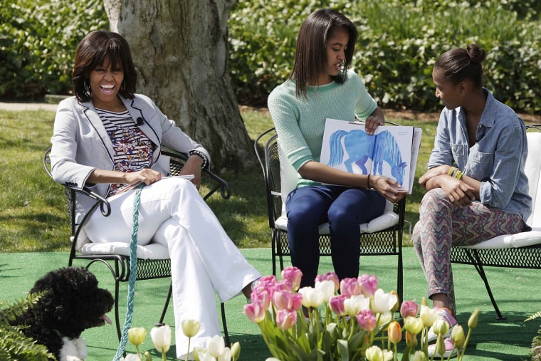 Image: U.S. first lady Michelle Obama smiles as her daughters Malia and Sasha read a children's book to kids during the annual Easter Egg Roll on the South Lawn of the White House in Washington